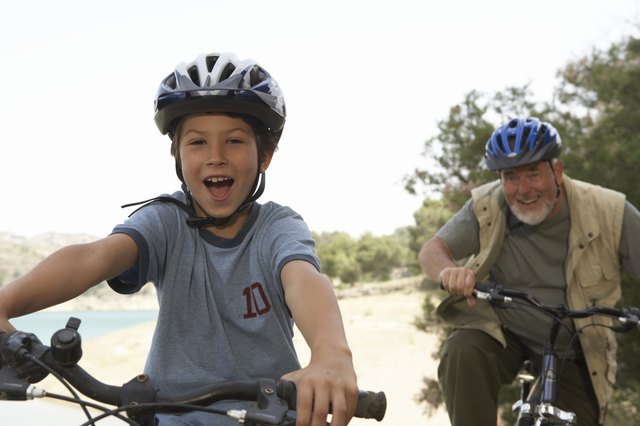 Grandson (5-7) and grandfather riding bikes, portrait (focus on boy)
