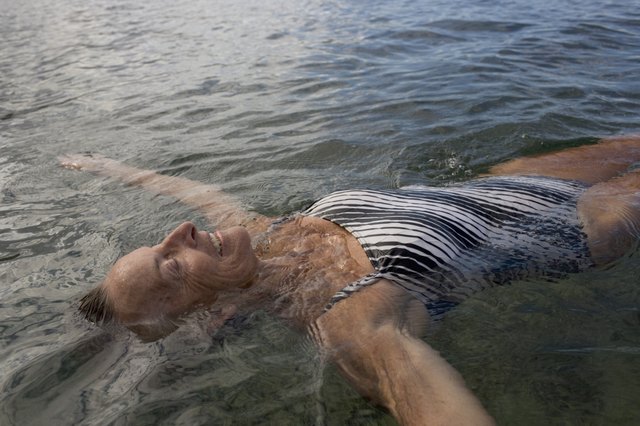 Senior woman floating in pool, arms outstretched, smiling, close-up