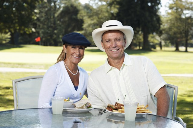 Mature couple sitting at outdoor table on golf course, portrait