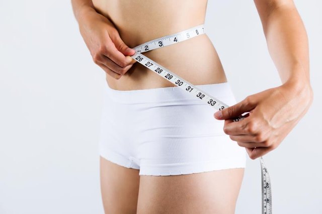 Portrait of woman measuring her slim body. Isolated on white background.