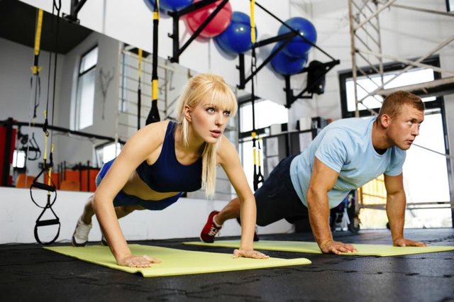 Photo of a woman doing pushups in a gym withe her personal trainer