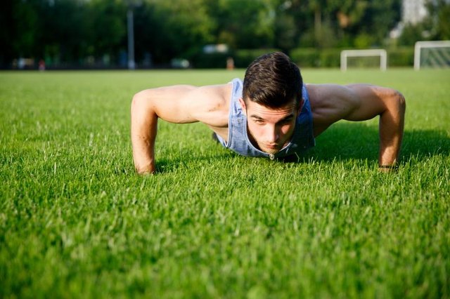Athletic young man doing push-ups on green grass on summer day.