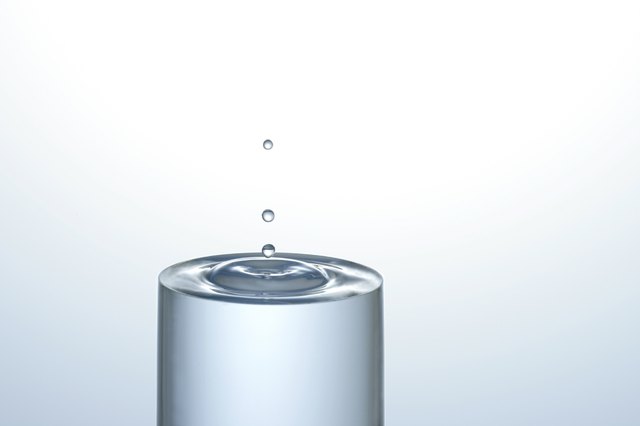 Water dropping onto a full glass of water, creating concentric circles on the surface
