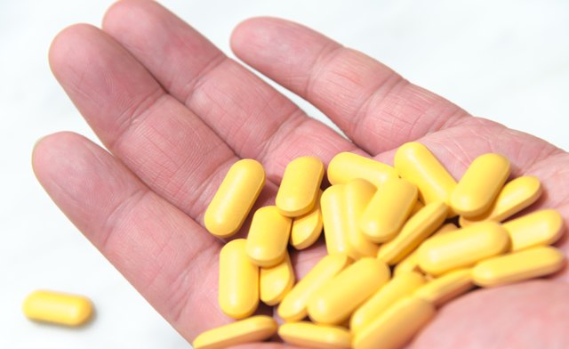 Chubby male's hand hold yellow vitamin tabletss