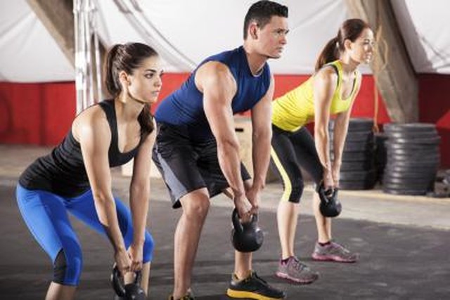 Three people working out with kettlebells in a gym gym