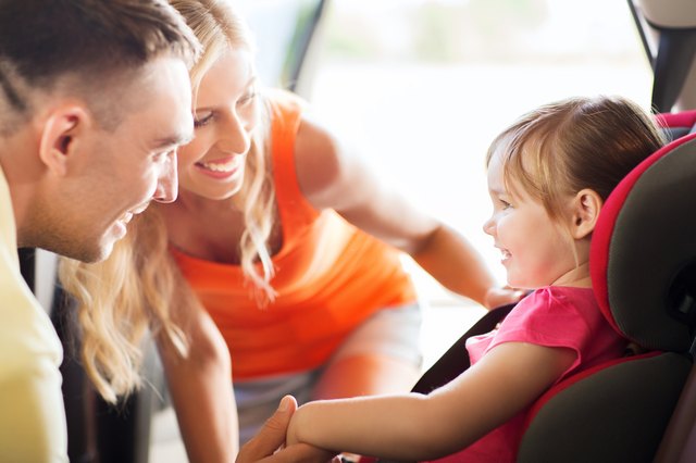 parents talking to little girl in baby car seat