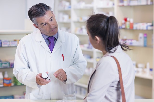 Pharmacist holding a bottle of drugs talking to customer