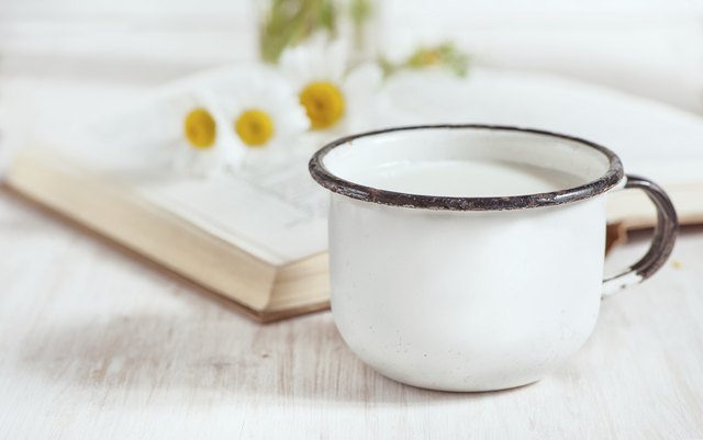Milk in metal mug and chamomile flowers on open book