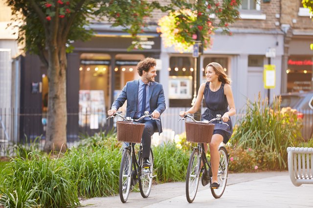Happy business people riding bikes through city park