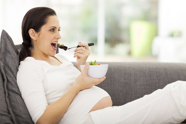 pregnant woman eating vegetables on sofa