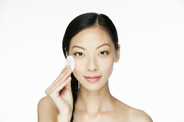 Young woman using cotton pad on face.