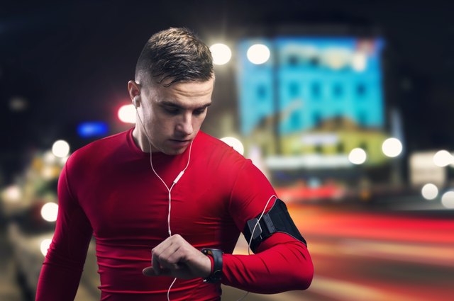 Man in red jogging at night and looking at his watch