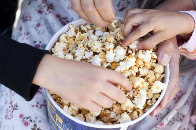Children eat popcorn out of a paper bucket, close-up