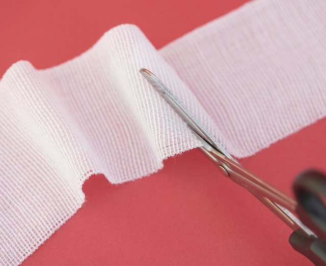 Pair of scissors cutting into strip of gauze, close-up