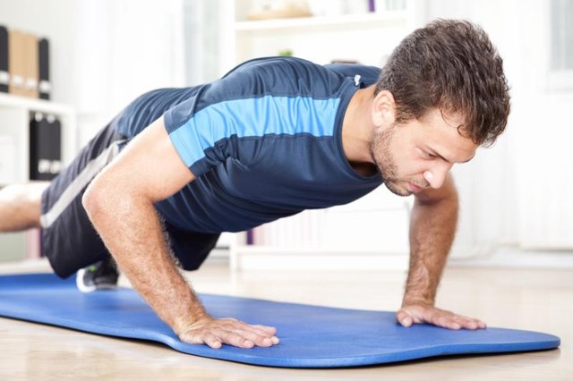 Fit Young Man Doing Indoor Planking Exercise on a Mat at Home, Showing Full Determination Expression.