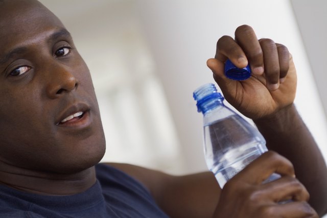 Bald man holding bottle of water with cap off, close-up, part of