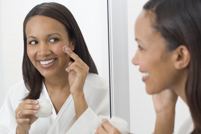 African woman applying face cream in mirror