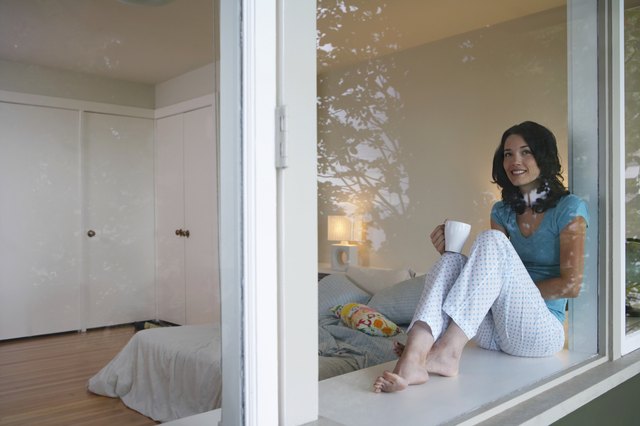 Woman sitting on windows sill, drinking coffee, smiling