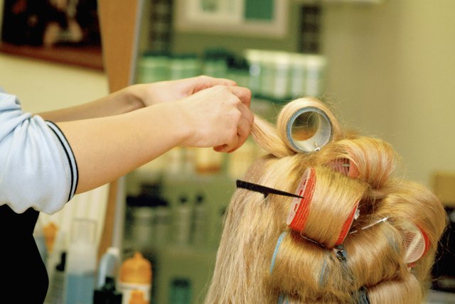 Close-up of a female hairdresser adjusting curlers in a mid adult woman's hair