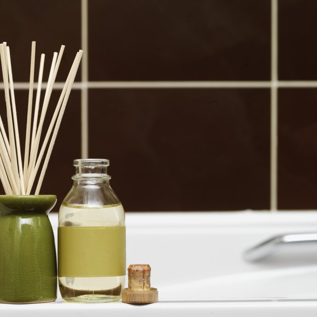 Close-up of incense sticks in a burner with a bottle of oil on side of bathtub