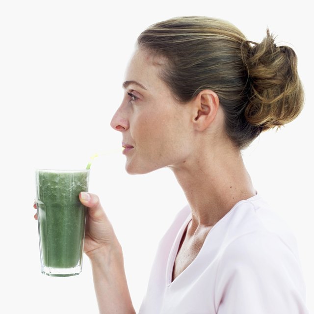 side view of a woman drinking a glass of thick green vegetable juice with a straw