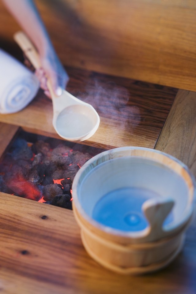 Person pouring water onto hot rocks in sauna