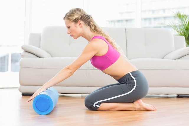 Fit blonde kneeling on floor using foam roller