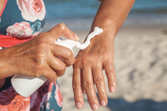 Elderly woman in swimsuit using cream for hand on beach