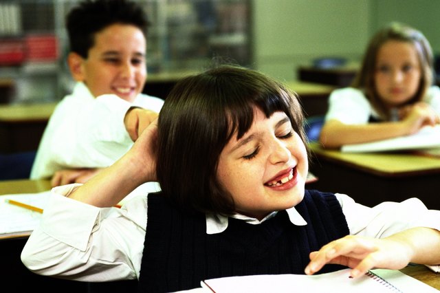 portrait of a school boy (8-10) pulling a girls hair in class