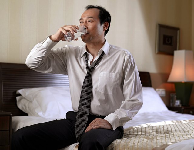 Businessman drinking water while sitting on bed.