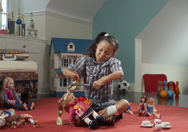 Girl (6-7 years) in room, cutting doll's hair