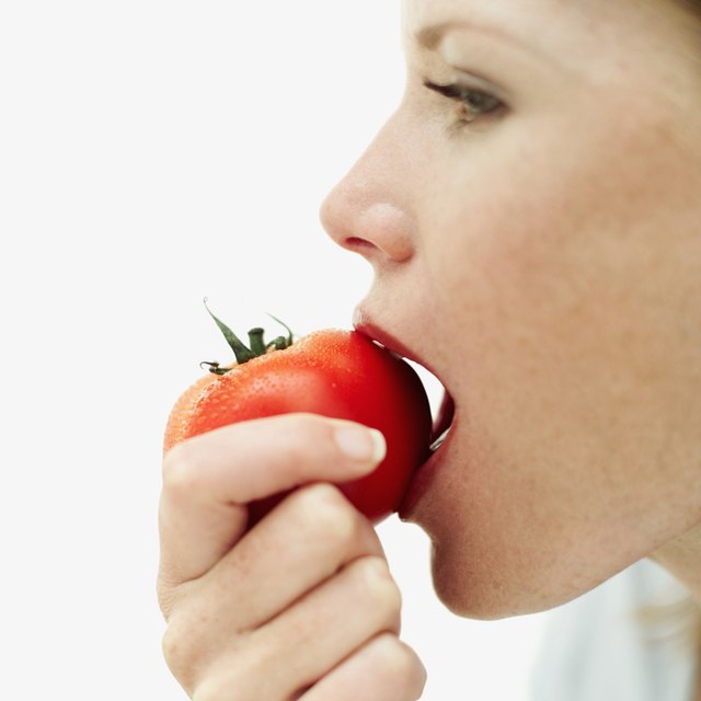 side profile of a young woman biting into a tomato