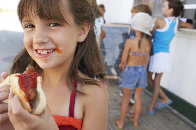 Girl (8-10) holding hotdog, sauce around mouth, smiling, portrait