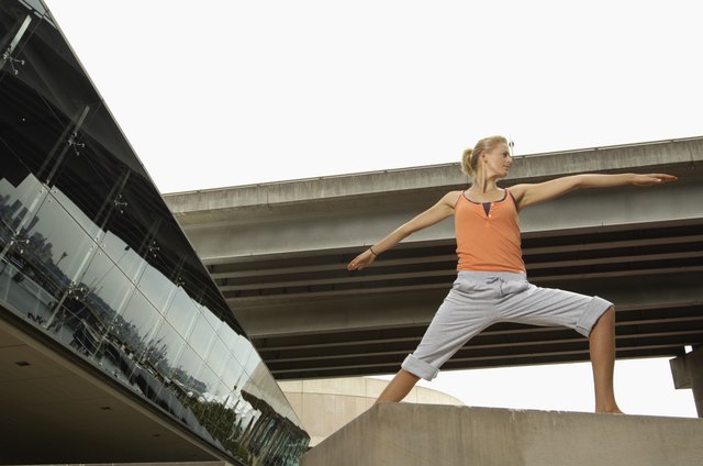 Young woman doing warrior 2 pose on concrete block, low angle