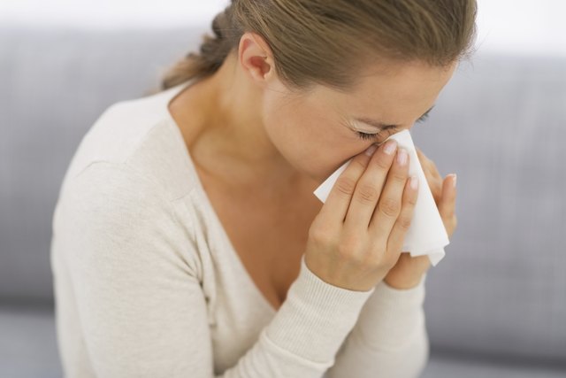 young woman sitting on couch and blowing nose