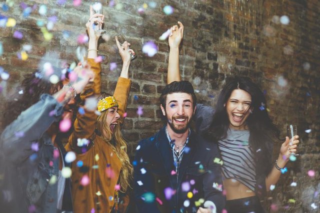 Group of four friends laughing out loud outdoor, sharing good and positive mood. Making party outdoor with champagne and confetti