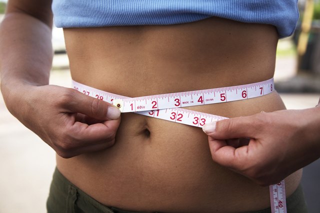 Mid section view of a woman measuring her waist with a tape measure