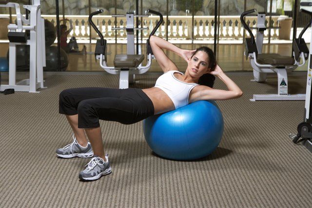 Woman doing exercise on fitness ball in gym, side view