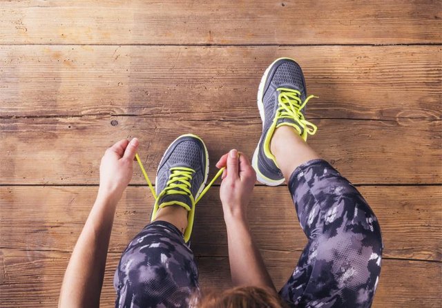 Unrecognizable young runner tying her shoelaces. Studio shot on wooden floor background.