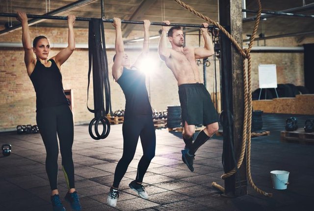 Fit young people doing pullups looking determined, working out in a gym