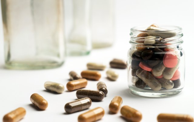 Different pills and capsules in glass jar on white background.