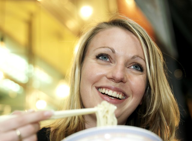 Woman eating noodles, smiling, low angle view