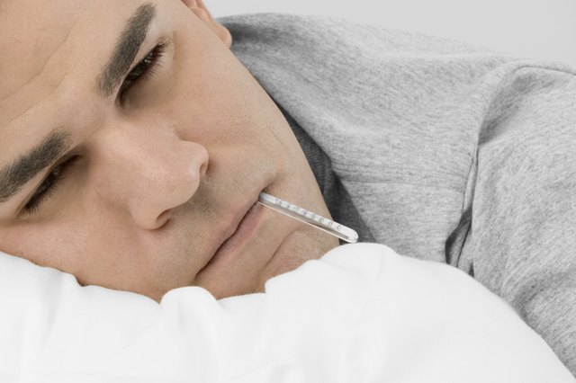 Mid adult man in bed with thermometer in mouth