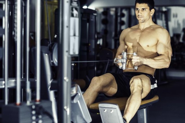 Man exercising back muscles on rowing machineMuscular young man exercising on rowing machine in modern gym.