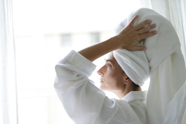 Woman with towel on head near window.