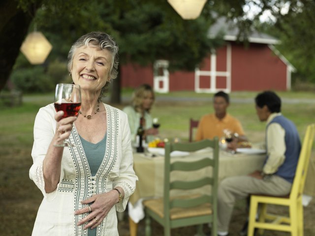 People dining in yard, focus on woman with red wine in foreground