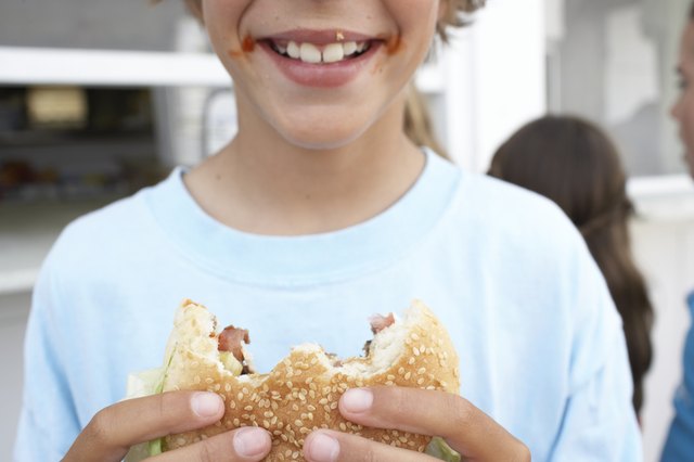 Boy (9-11) holding hamburger with 'bites' missing, smiling, close-up