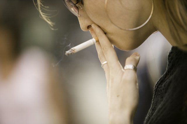 Young woman wearing sunglasses, smoking outdoors, close-up