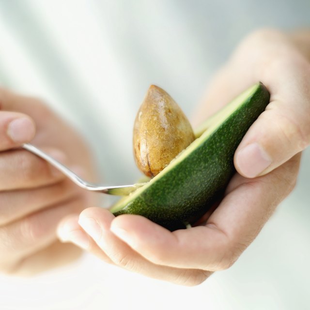 close-up of a person's hand scooping out the seed of an avocado with a spoon