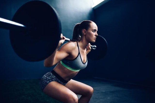 Young female athlete doing squat with barbell in gym gym